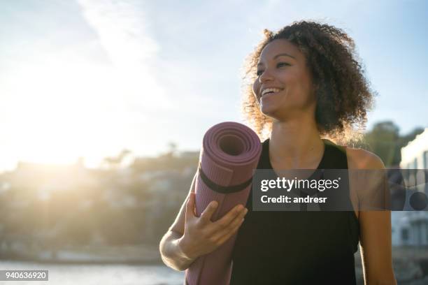 donna in forma che tiene in mano un tappetino da yoga in spiaggia - sunrise yoga foto e immagini stock