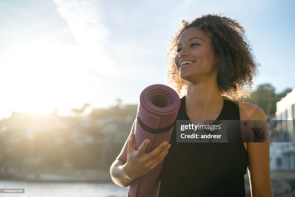 Fit woman holding a yoga mat at the beach
