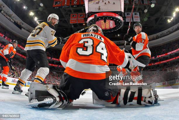 Petr Mrazek of the Philadelphia Flyers lets the puck fall between his pads as Andrew MacDonald and Patrice Bergeron of the Boston Bruins look back...