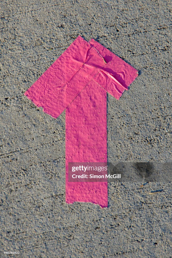 Arrow made from pink duct tape on a concrete footpath