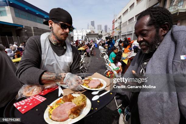 Volunteer Brian Burnham, left, hands out plates of food to hundreds of homeless and near-homeless men and women and children who enjoy an Easter...