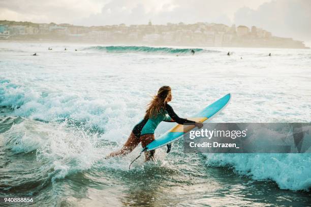 woman surfer jumps on her surfboard in the wave - sydney morning stock pictures, royalty-free photos & images
