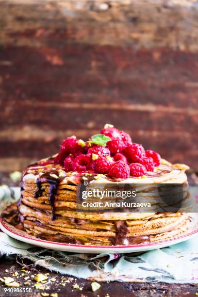 stack of wheat golden pancakes or pancake cake with freshly picked raspberry, chopped pistachios, chocolate sauce on a dessert plate, selective focus - raspberry sauce stock pictures, royalty-free photos & images