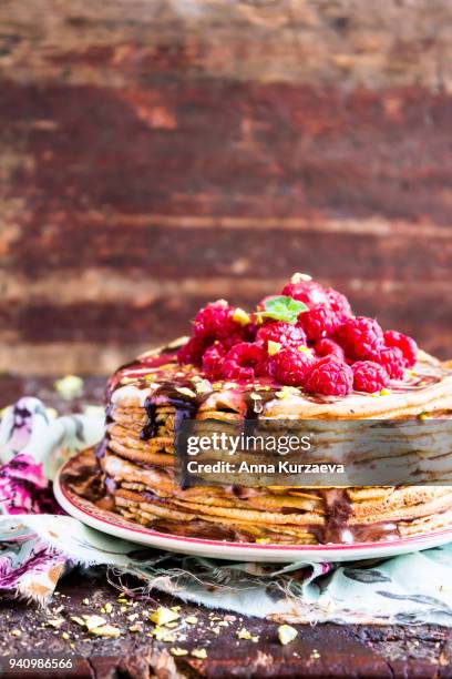 stack of wheat golden pancakes or pancake cake with freshly picked raspberry, chopped pistachios, chocolate sauce on a dessert plate, selective focus - raspberry sauce stock pictures, royalty-free photos & images