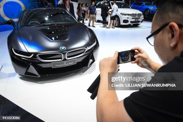 Man takes a photo of a BMW i8 hybrid sports car during the annual Bangkok International Motorshow in Bangkok on April 2, 2018. / AFP PHOTO / LILLIAN...