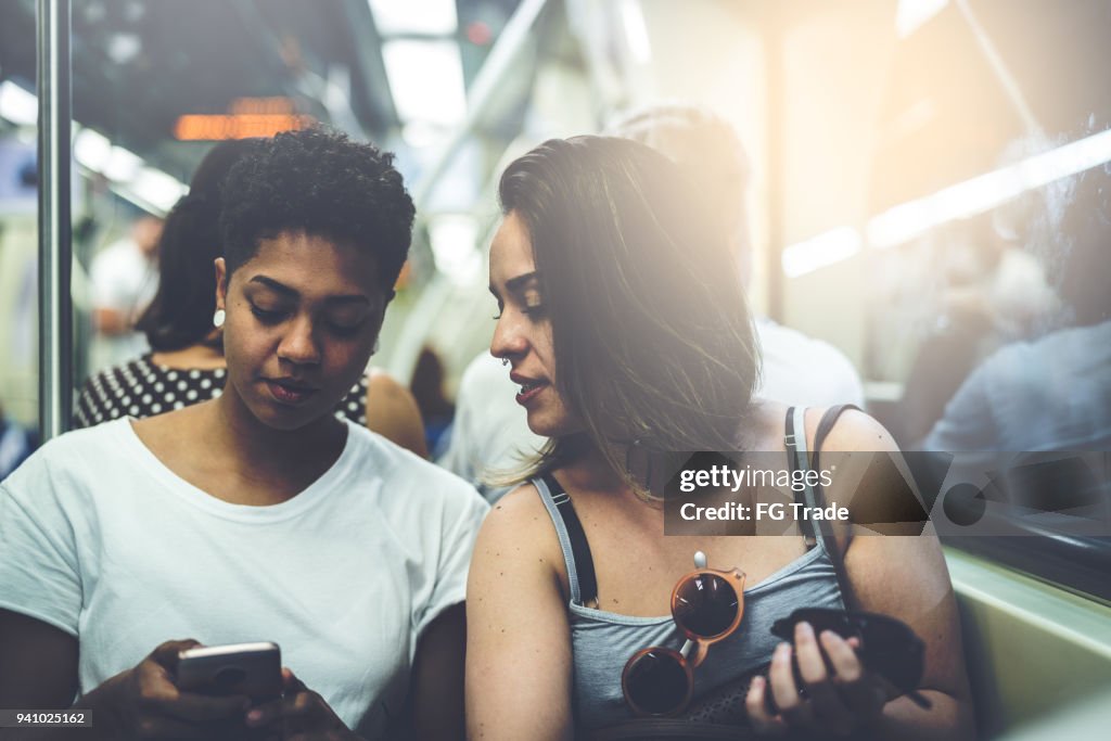 Casal de lésbicas usando o celular no metrô