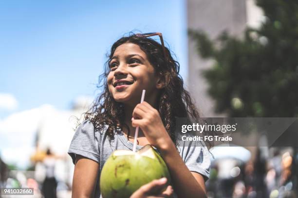 cute young girl drinking coconut water on a city break - coconut water stock pictures, royalty-free photos & images