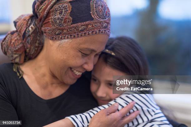 senior mujer étnica con cáncer se sienta por su ventana con su nieta - cancer survivor fotografías e imágenes de stock