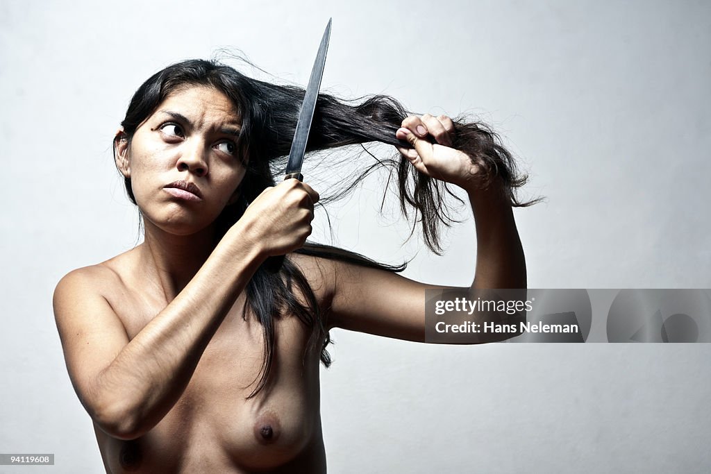 Close-up of a naked woman cutting hair with a knife