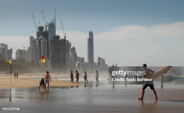 Lifeguard walks along the beach with a surfboard as people swim between the flags ahead of the 2018 Commonwealth Games on April 3, 2018 in the Gold...