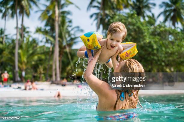 happy little boy having fun in the sea while being held by his mother. - beach holiday stock pictures, royalty-free photos & images