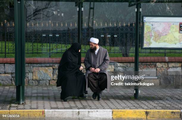 muslim religious couple waiting for bus at busstop by bosphorus strait near rumelikavagi beykoz istanbul turkey - imam stock pictures, royalty-free photos & images
