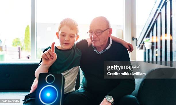 junge veranschaulicht großeltern, einen digitalen assistent mit sprachbefehlen zu verwenden - mikkelwilliam stock-fotos und bilder