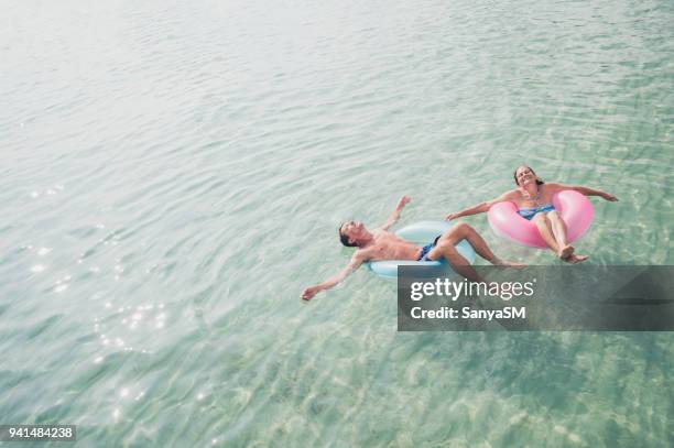 senior couple enjoy sea water - man on float stock pictures, royalty-free photos & images