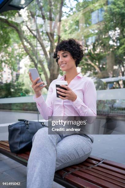 femme d’affaires en attente d’un bus et envoyer des sms sur son téléphone cellulaire à l’arrêt de bus - sms'en photos et images de collection