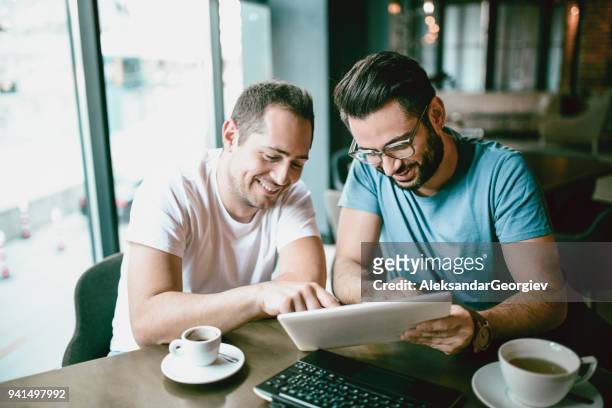 handsome smiling freelancer showing finished project on digital tablet to a colleague in coffee restaurant - ciber café imagens e fotografias de stock