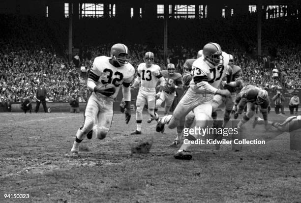 Runningback Jim Brown of the Cleveland Browns runs on a sweep behind tackle Monte Clark as quarterback Frank Ryan watches from the back of the play...