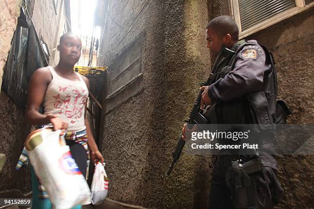 Woman passes a member of Special Police Operations Battalion while they search homes for guns and drugs in the slum, or favela, Cantagalo in...