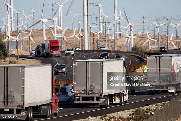Emissions-producing diesel trucks and cars pass non-polluting windmills along the 10 freeway on December 8, 2009 near Banning, California. Sustained...