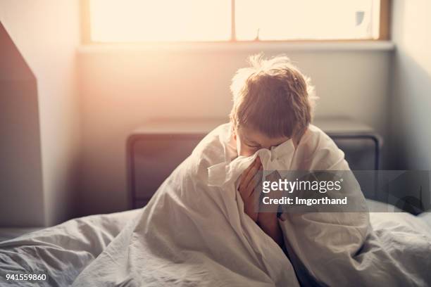 sick little boy lying in bed and blowing nose - illness stock pictures, royalty-free photos & images