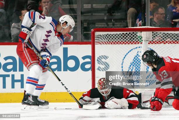 Keith Kinkaid of the New Jersey Devils covers the puck during the second period as Peter Holland of the New York Rangers looks for a rebound at the...