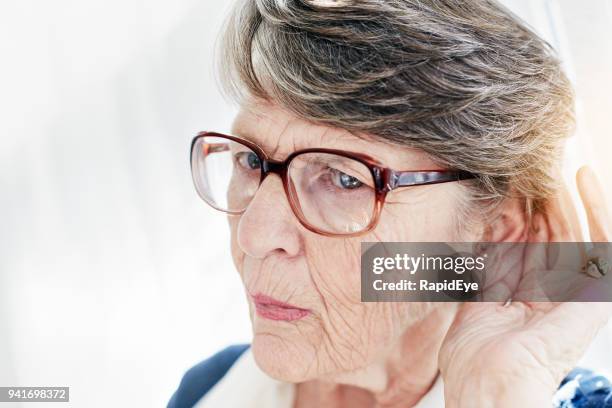 deaf old woman frowns, cupping ear and trying to hear - old woman covering ears stock pictures, royalty-free photos & images