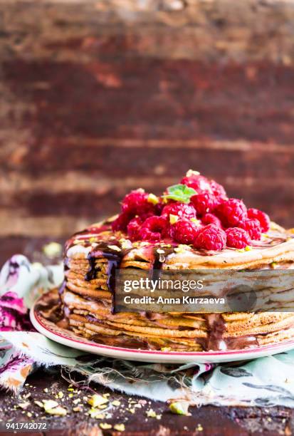 stack of wheat golden pancakes or pancake cake with freshly picked raspberry, chopped pistachios, chocolate sauce on a dessert plate, selective focus - raspberry sauce stock pictures, royalty-free photos & images