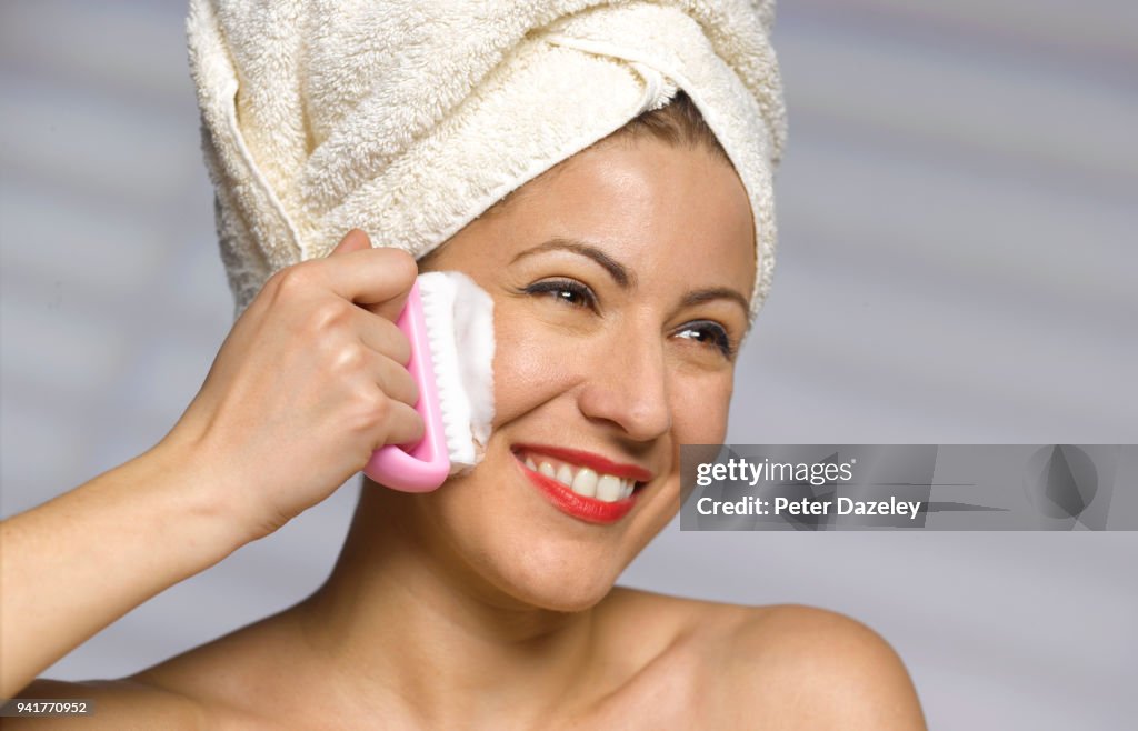 WOMAN EXFOLIATING FACE WITH NAIL BRUSH