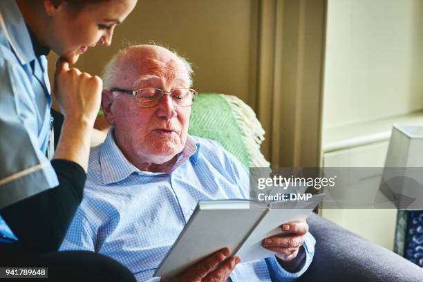 mature man reading a book with home caregiver - palliative care stock pictures, royalty-free photos & images