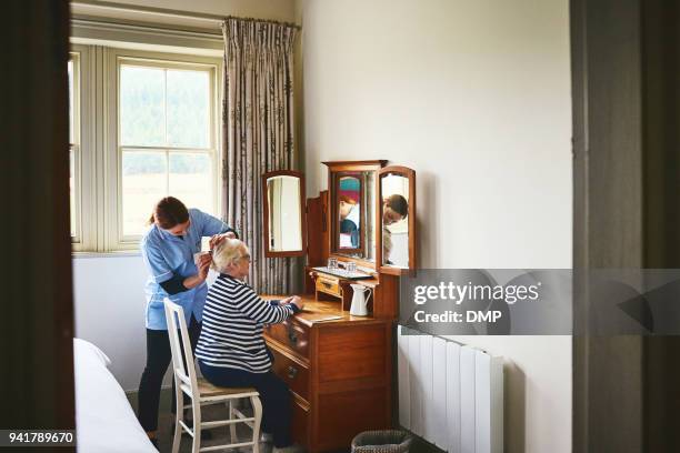 verpleegster aankleden van de haren van een senior vrouw - nurse helping old woman at home stockfoto's en -beelden