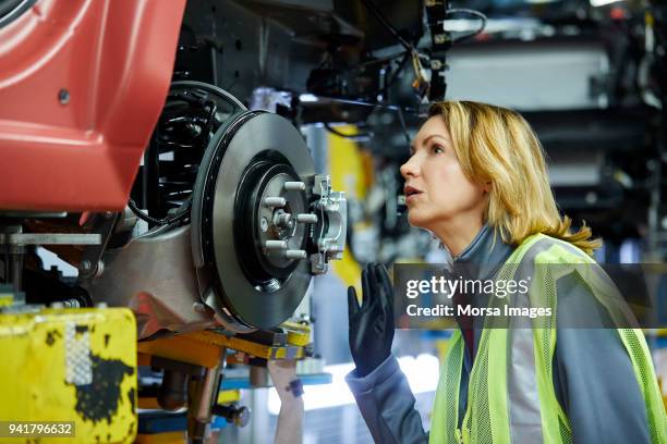 blond vrouwelijke ingenieur controleren voertuig in fabriek - motorvoertuig stockfoto's en -beelden