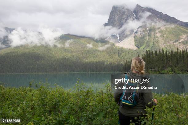 woman stands at edge of lake in the mountains - heavy rucksack stock pictures, royalty-free photos & images