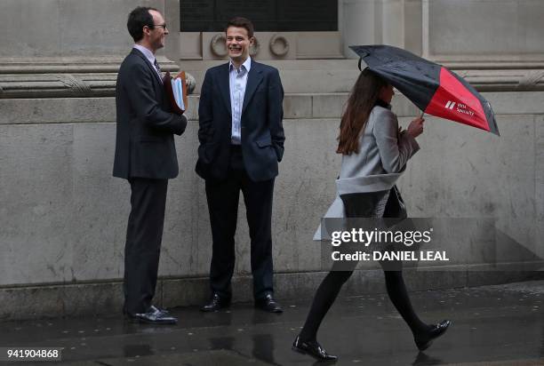 Woman shelters from the rain beneath an umbrella as she walks past talking men in the City of London on April 4, 2018. - Employers with more than 250...