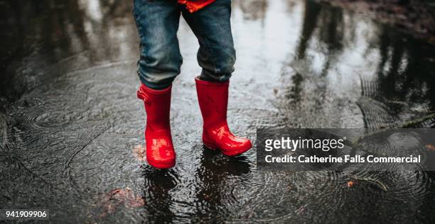 child jumping in a big puddle - red shoe stock-fotos und bilder