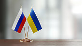 Russian And Ukrainian Flag Pair On A Desk Over Defocused Background