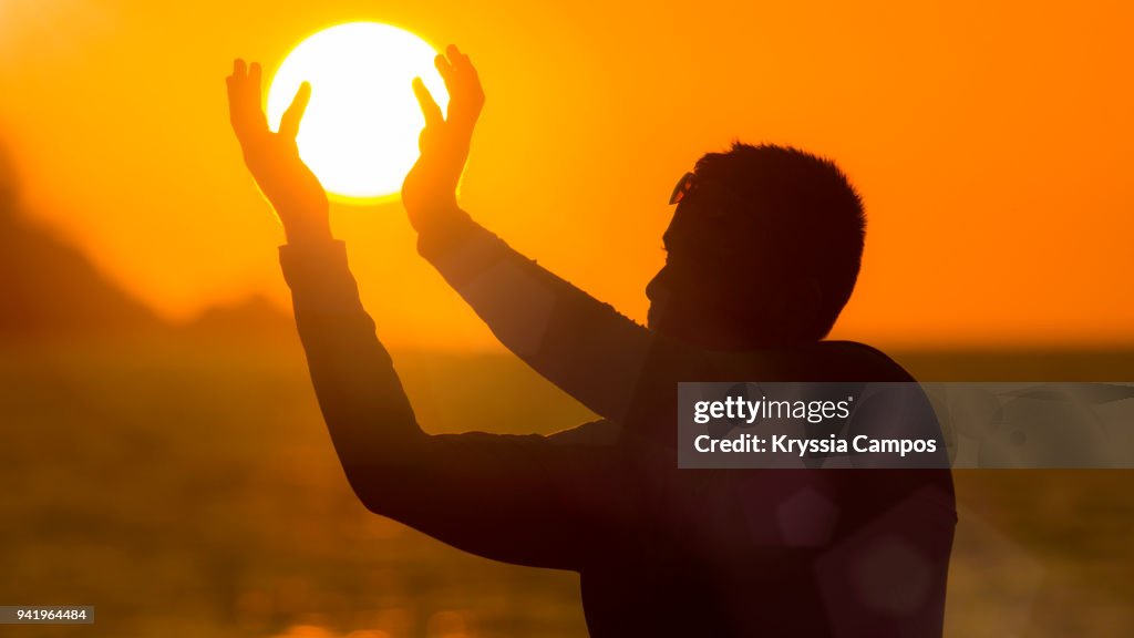 Optical Illusion Of Man Holding Sun At Beach During Sunset