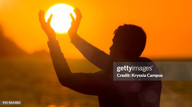 optical illusion of man holding sun at beach during sunset - playa tamarindo - fotografias e filmes do acervo