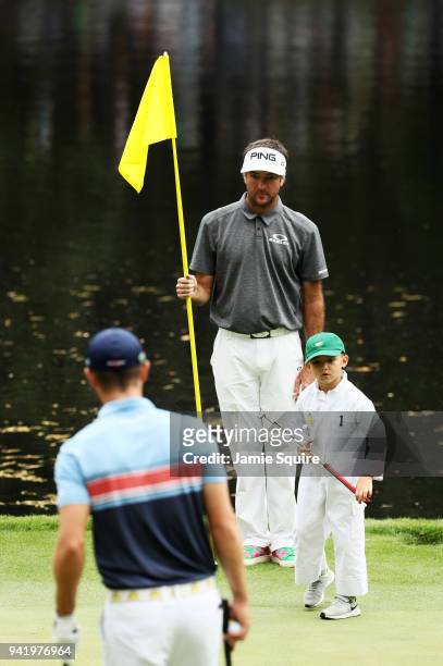 Bubba Watson of the United States holds the flag alongside son Caleb as Wesley Bryan of the United States looks on during the Par 3 Contest prior to...