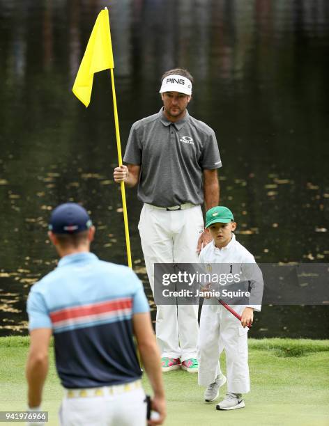 Bubba Watson of the United States holds the flag alongside son Caleb as Wesley Bryan of the United States looks on during the Par 3 Contest prior to...