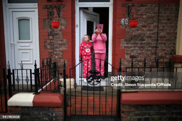 Woman and her daughter stand in their doorway wearing pyjamas as they film fans passing by in the street prior to the UEFA Champions League Quarter...