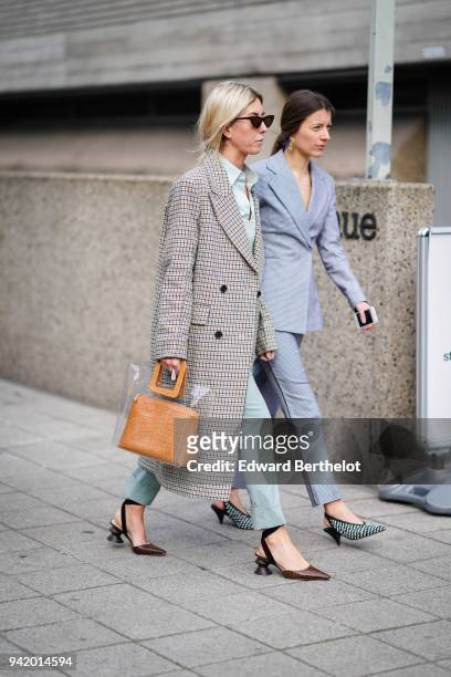 Guest wears a checked coat, a brown bag in a transparent pvc bag, blue pants, shoes, during London Fashion Week February 2018 on February 18, 2018 in...