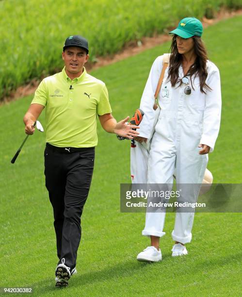 Rickie Fowler of the United States walks with caddie and girlfriend Allison Stokke during the Par 3 Contest prior to the start of the 2018 Masters...