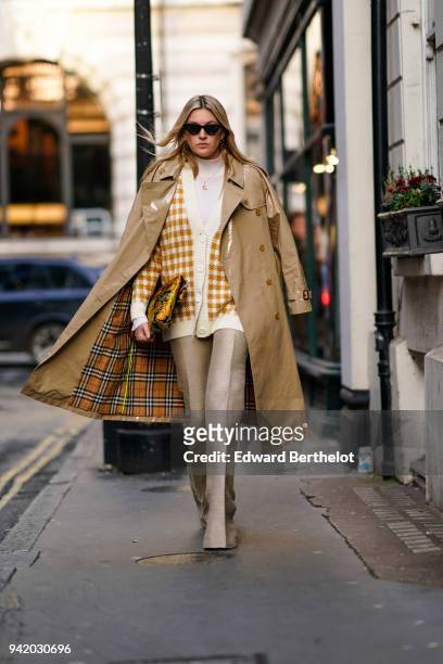 Camille Charriere wears a trench coat, a checked jacket, flare pants, sunglasses, during London Fashion Week February 2018 on February 16, 2018 in...