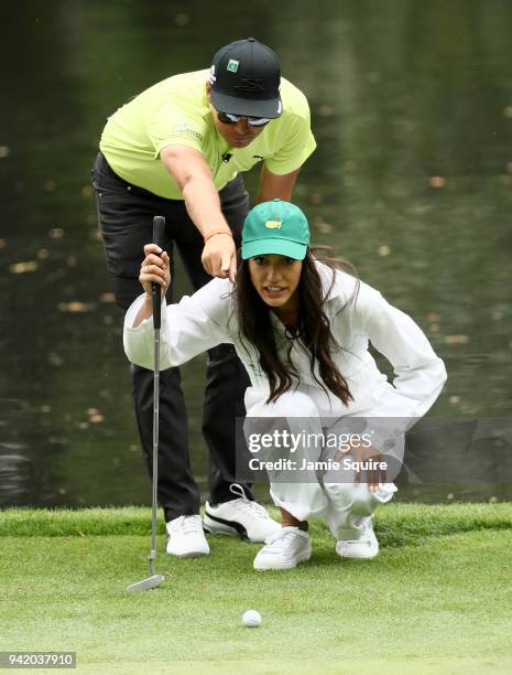 Rickie Fowler of the United States lines up a putt with girlfriend Allison Stokke during the Par 3 Contest prior to the start of the 2018 Masters...