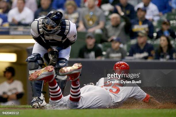 Dexter Fowler of the St. Louis Cardinals slides into home plate to score a run past Manny Pina of the Milwaukee Brewers in the first inning at Miller...