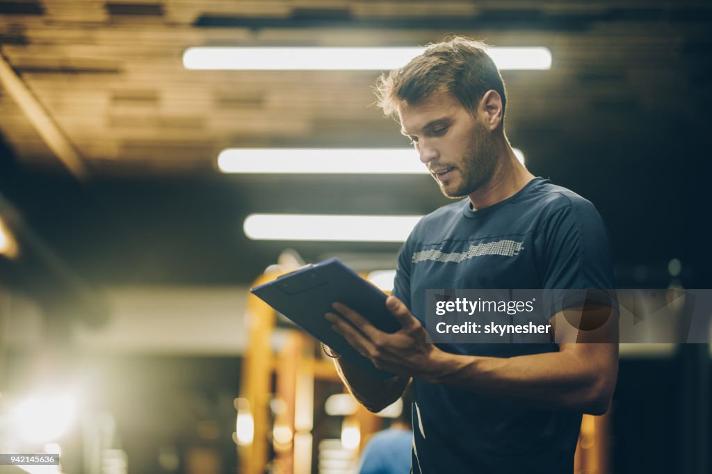 Young fitness instructor reading a training plan in a gym.