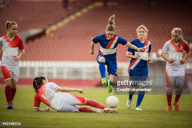 female soccer player jumping over her opponent during a match on a stadium. - tackling stock pictures, royalty-free photos & images