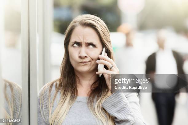 gefrustreerd vrouw in de straat luisteren op telefoon rolt haar ogen - rollen met de ogen stockfoto's en -beelden