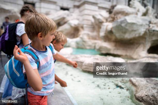 los niños a los turistas lanzan monedas a la fontana de trevi, roma - fontana de trevi fotografías e imágenes de stock