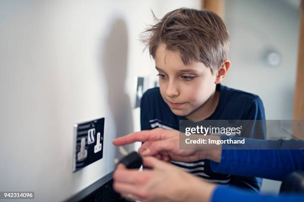 moeder uit te leggen van elektriciteits- en stopcontact aan haar zoon - electrical shock stockfoto's en -beelden